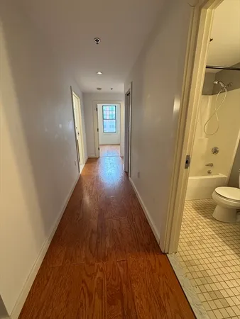a view of a hallway with wooden floor and a bathroom