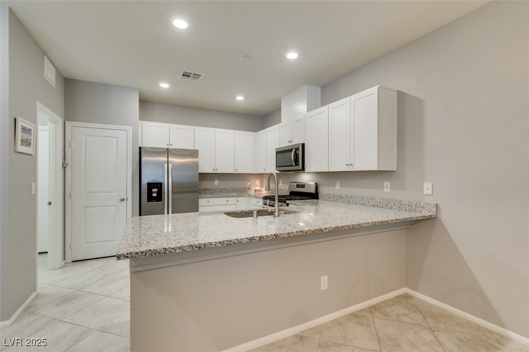 2870 Turnstone Ridge Street Henderson, NV 89044 - Photo 22 of 50 Kitchen featuring stainless steel appliances, a sink, a peninsula, light stone counters, and white cabinets