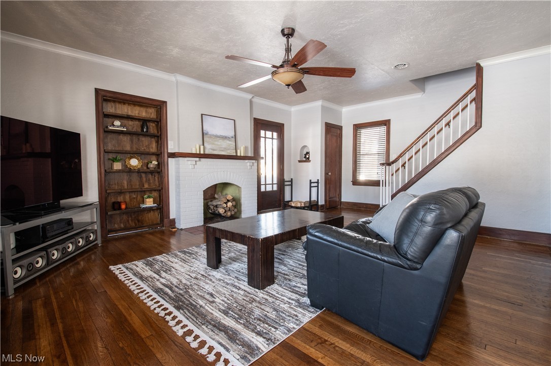 Living room with a fireplace, crown molding, ceiling fan, a textured ceiling, and dark hardwood / wood-style flooring