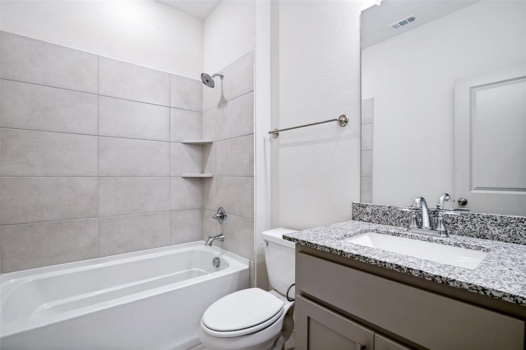 1006 Emil Place Allen, TX 75013 - Photo 18 of 28 Bathroom featuring a bathtub with tiled surround and integrated shelving, granite-finish countertop, under-mount sink, and chrome fixtures