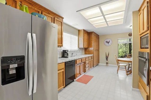 a kitchen with stainless steel appliances granite countertop a refrigerator a sink dishwasher a stove and white countertops with wooden floor