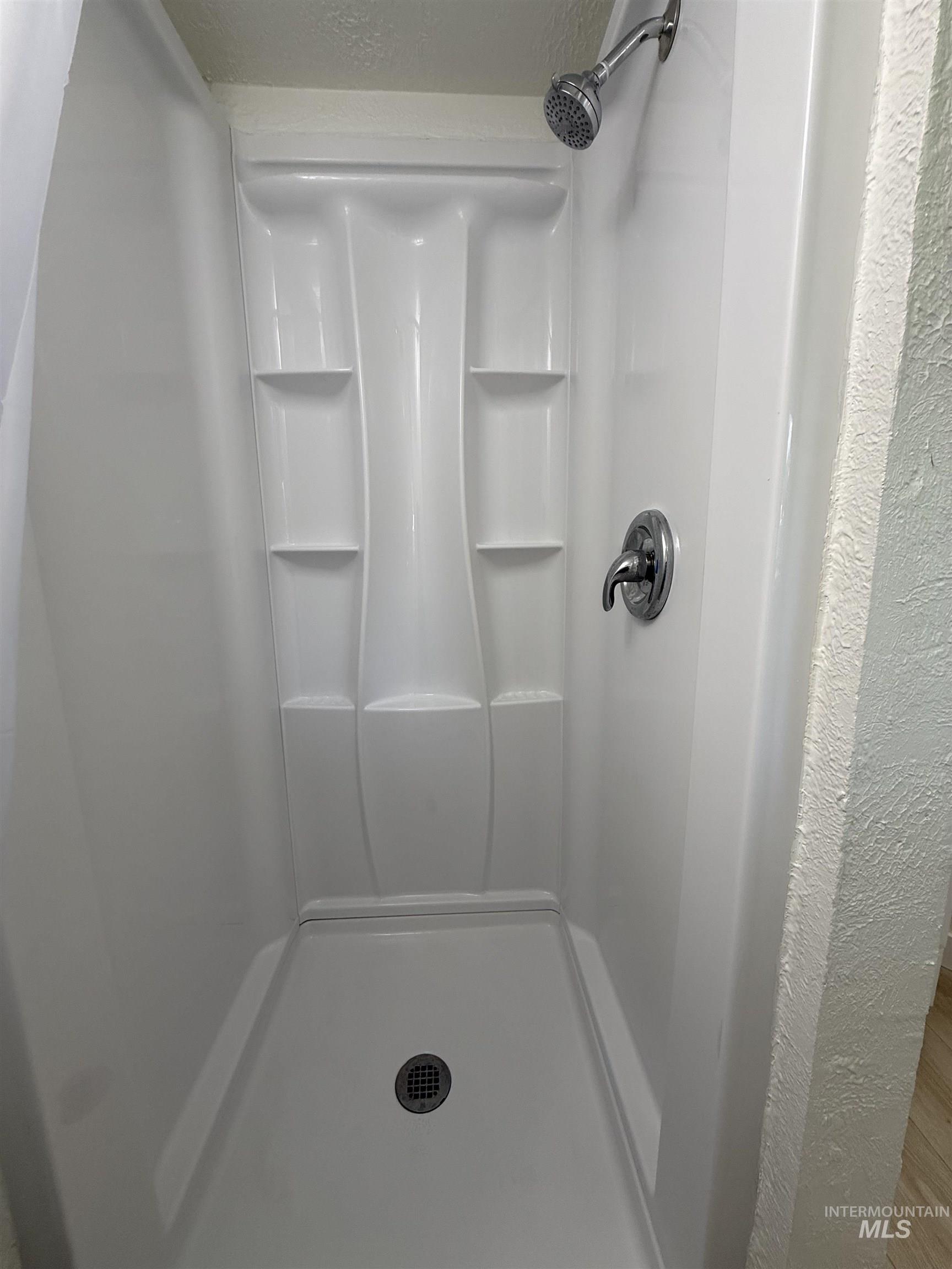 820 Nickle Street Kamiah, ID 83536 - Photo 19 of 26 White acrylic shower stall with integrated shelving, chrome shower head, and coordinating chrome fixtures