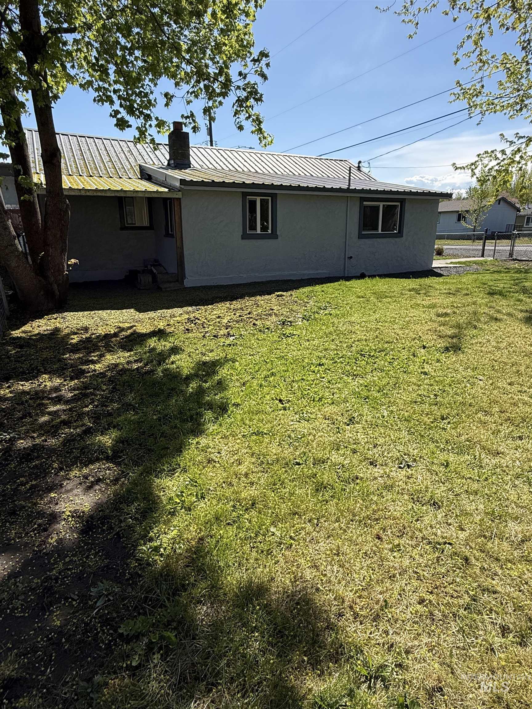 820 Nickle Street Kamiah, ID 83536 - Photo 5 of 26 Rear exterior featuring a metal roof, light gray stucco siding, and white-trimmed windows