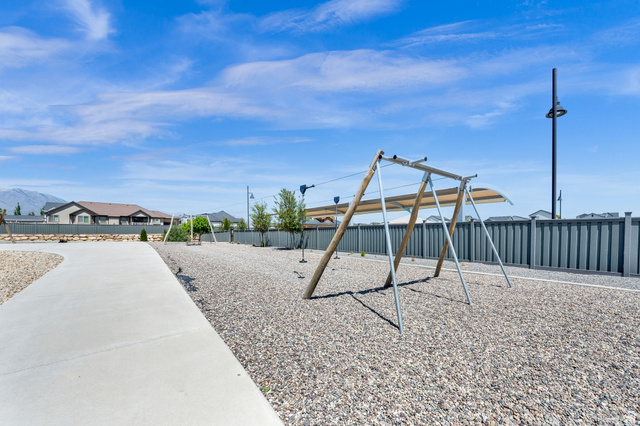 6120 North Sheps Ridge Road Eagle Mountain, UT 84005 - Photo 19 of 43 Outdoor recreational area featuring a gravel surface, playground equipment with sun shades, a concrete pathway, a privacy fence, and distant mountain scenery