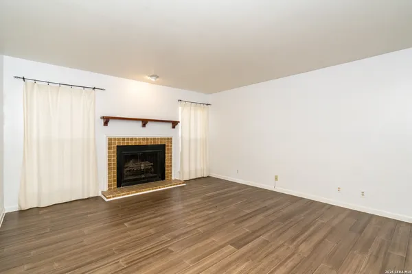 a view of an empty room with wooden floor fireplace and a window