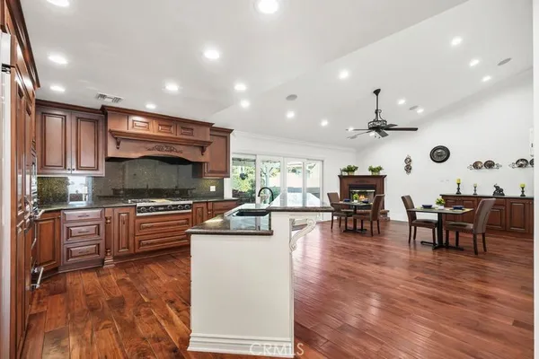 a kitchen with stainless steel appliances kitchen island granite countertop a stove top oven a sink a dining table and chairs with wooden floor