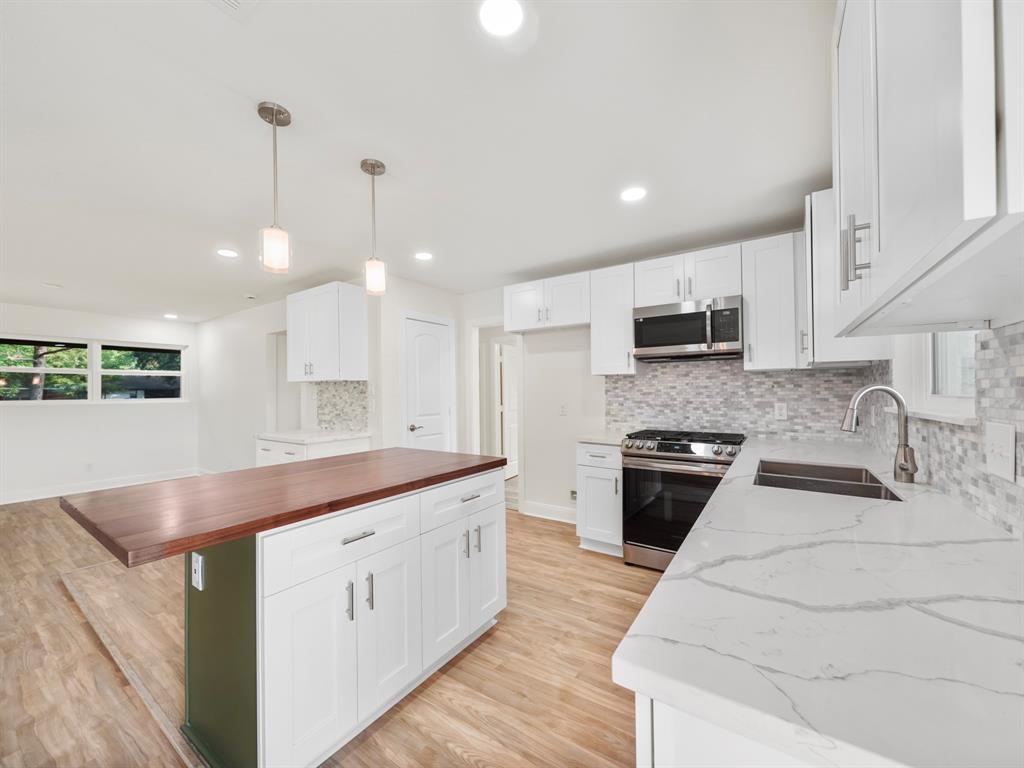 a large white kitchen with stainless steel appliances kitchen island granite countertop a stove a sink a refrigerator and white cabinets with wooden floor