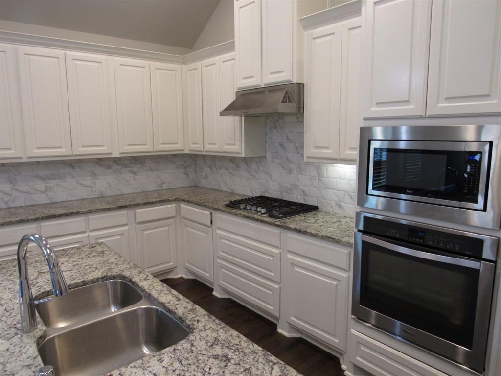 816 Pier Street Little Elm, TX 76227 - Photo 12 of 27 Kitchen with white cabinets, stainless steel appliances, vaulted ceiling, light stone counters, and dark wood finished floors