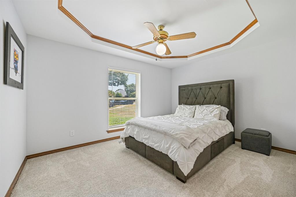 925 Spring Brook Drive Allen, TX 75002 - Photo 19 of 30 Spacious primary bedroom with wood-trim architectural ceiling detail, bronze ceiling fan with integrated lighting, upholstered headboard bed frame, and large window with pastoral landscape backdrop