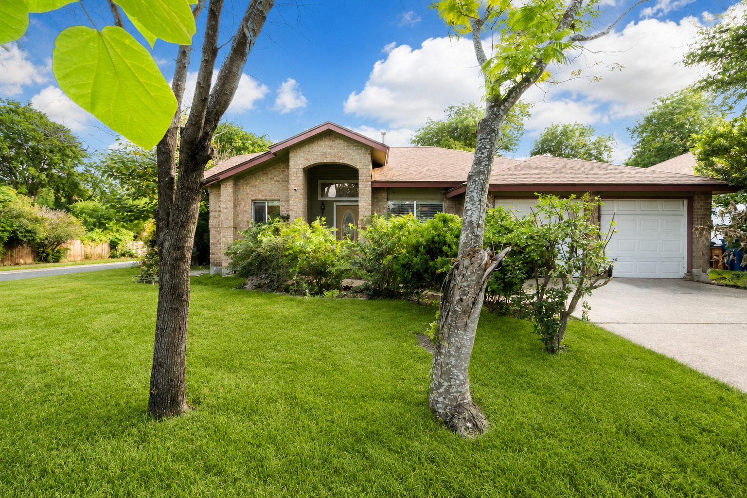5611 Meadow Crest Austin, TX 78744 - Photo 2 of 29 Mature trees and vibrant landscaping frame this inviting brick facade with an attached garage.