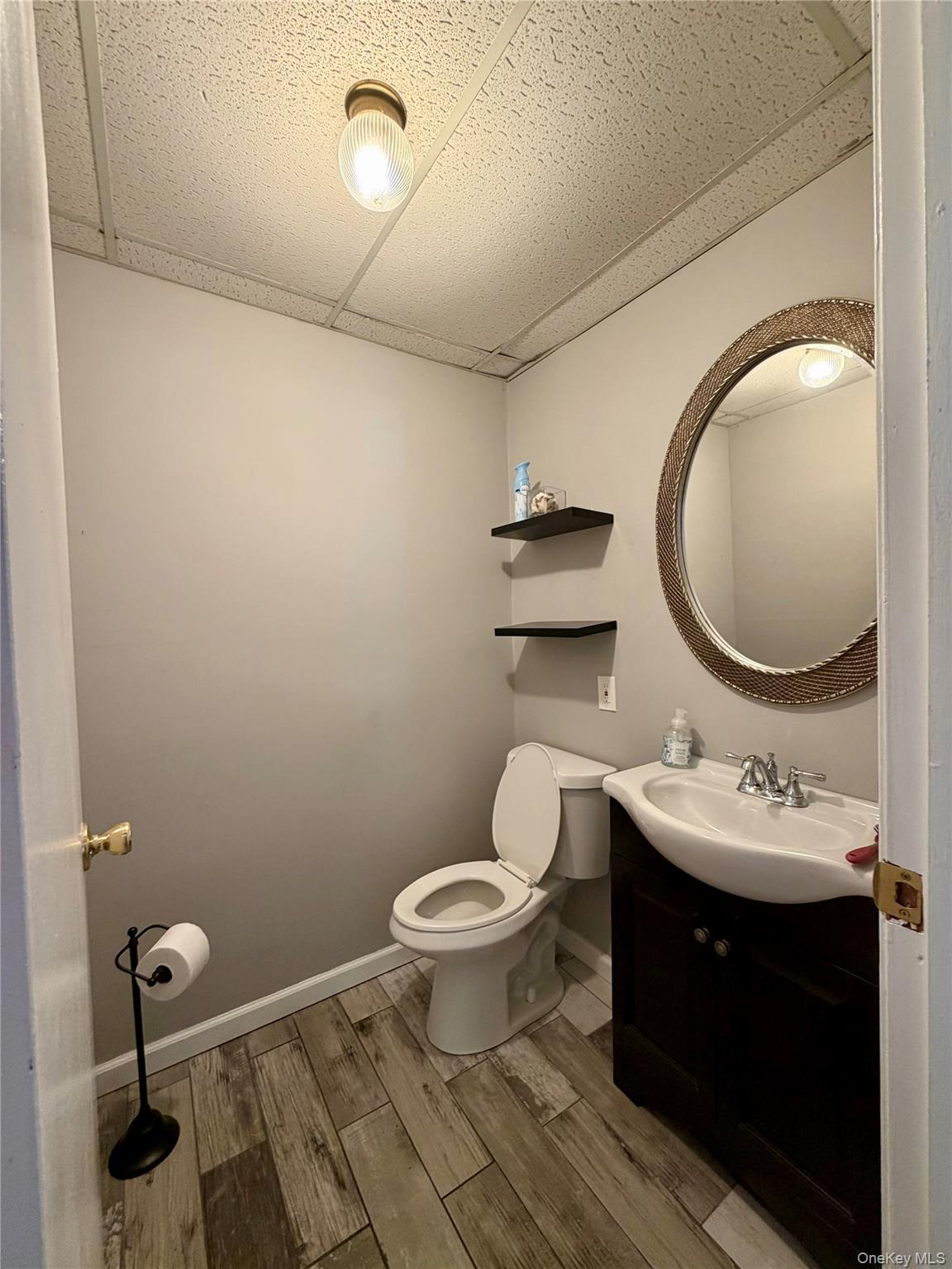 149 Fort Salonga Road Northport, NY 11768 - Photo 3 of 23 Bathroom featuring wood-finish flooring, a contemporary vanity with an integrated sink, a toilet, a decorative round mirror, and a drop ceiling with recessed lighting