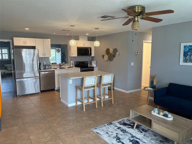 a kitchen with stainless steel appliances kitchen island granite countertop a refrigerator a stove a sink a dining table and chairs with wooden floor
