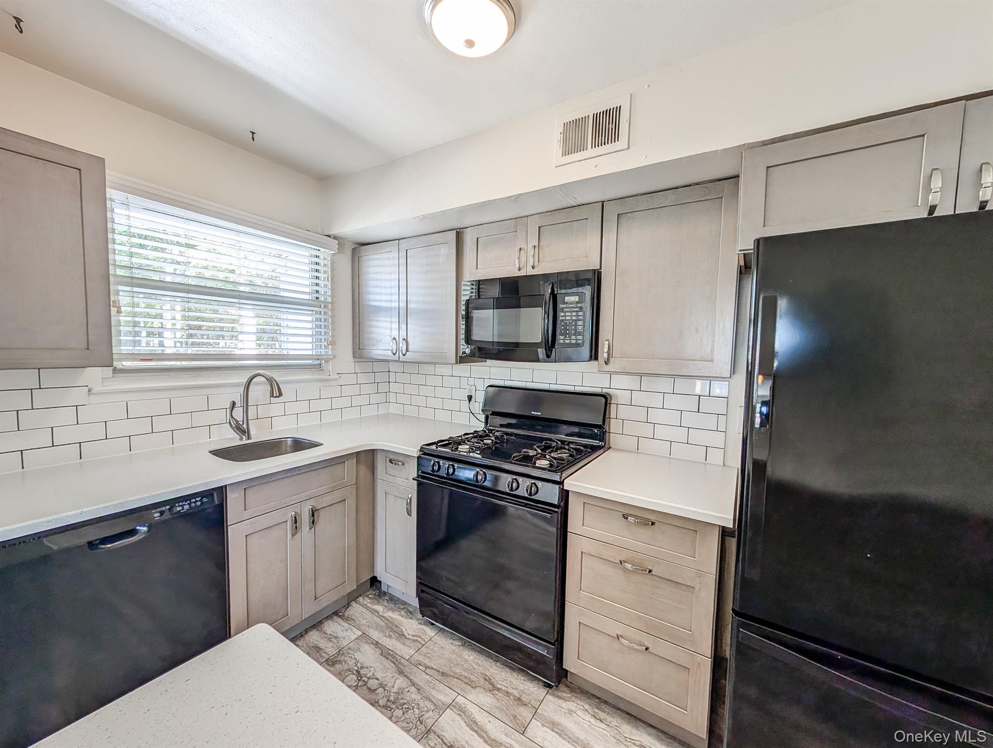 73 Rocky Point Yaphank Road, Unit 106 Rocky Point, NY 11778 - Photo 2 of 12 Kitchen featuring black appliances, backsplash, and light stone countertops