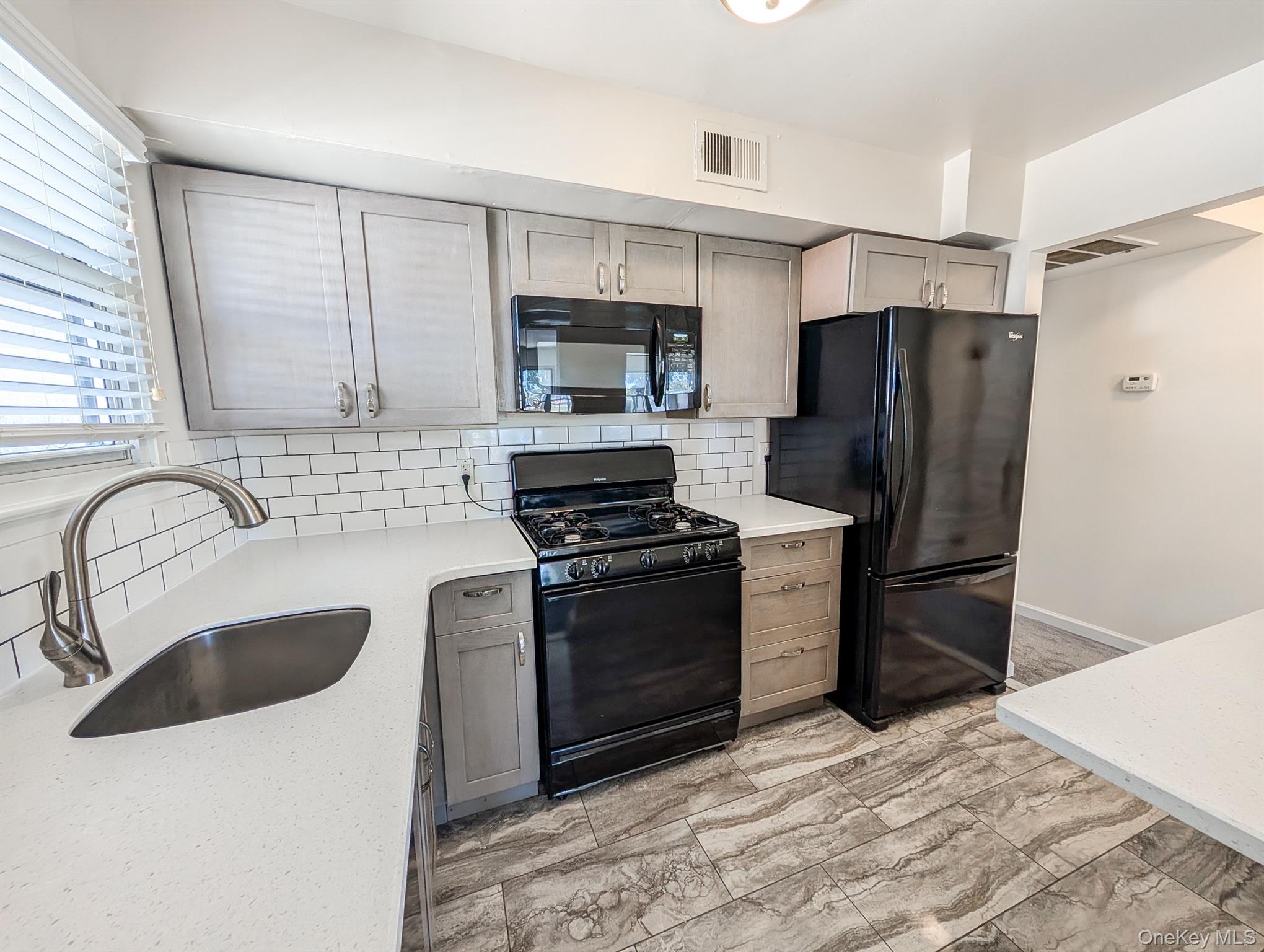 73 Rocky Point Yaphank Road, Unit 106 Rocky Point, NY 11778 - Photo 3 of 12 Kitchen with black appliances, decorative backsplash, light stone counters, light marble finish floors, and gray cabinetry