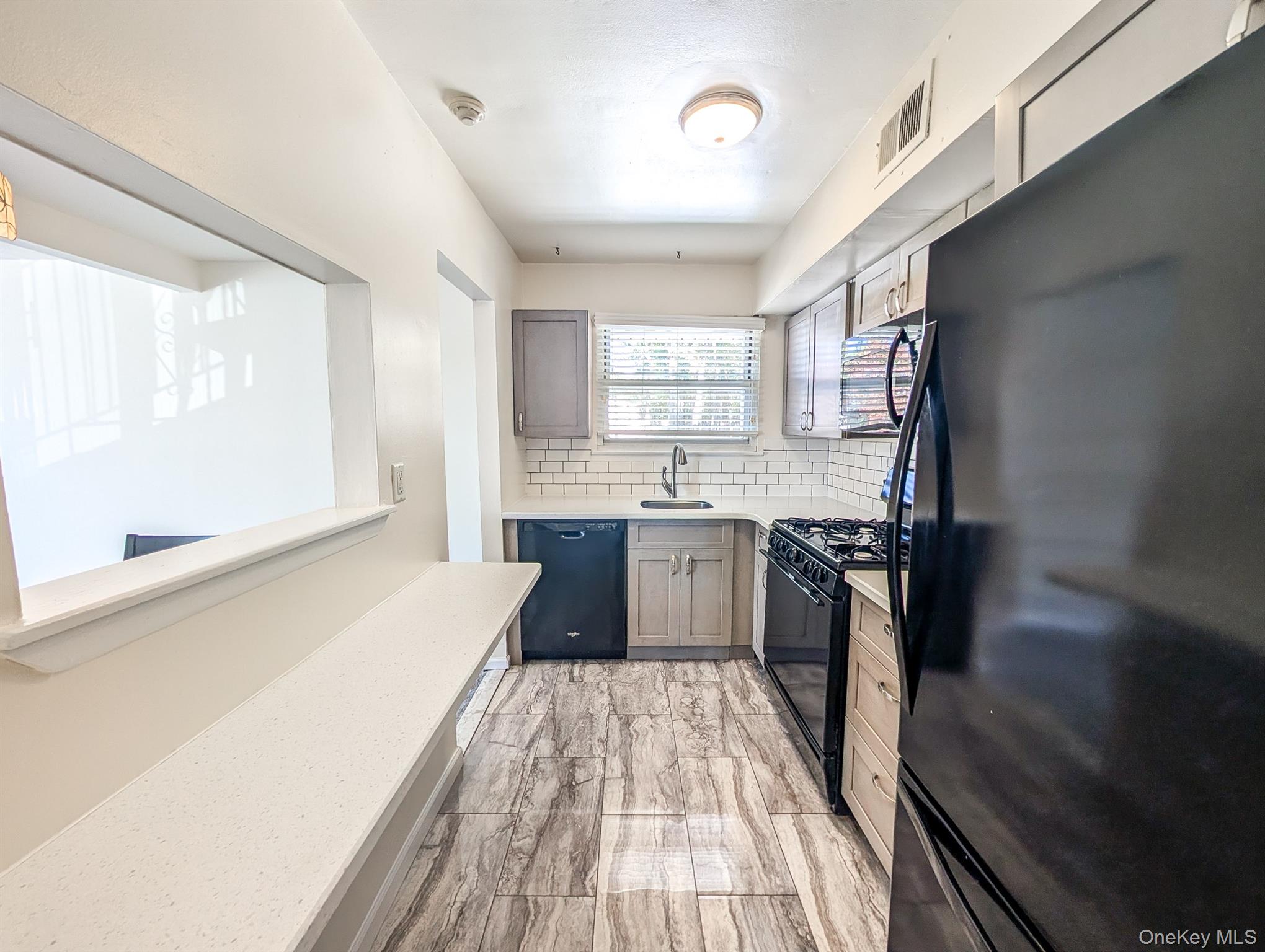 73 Rocky Point Yaphank Road, Unit 106 Rocky Point, NY 11778 - Photo 4 of 12 Kitchen featuring black appliances, backsplash, and light stone counters