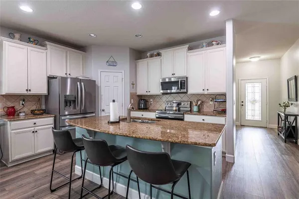 a kitchen with stainless steel appliances granite countertop a stove a sink a microwave a refrigerator white cabinets and wooden floor