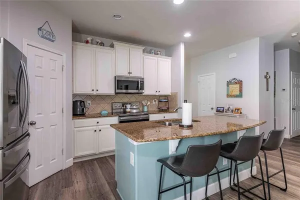 a kitchen with stainless steel appliances granite countertop a stove top oven a refrigerator a sink and white cabinets with wooden floor