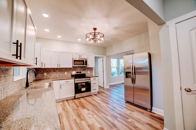 a kitchen with stainless steel appliances granite countertop a stove top oven a sink dishwasher and a refrigerator with wooden floor