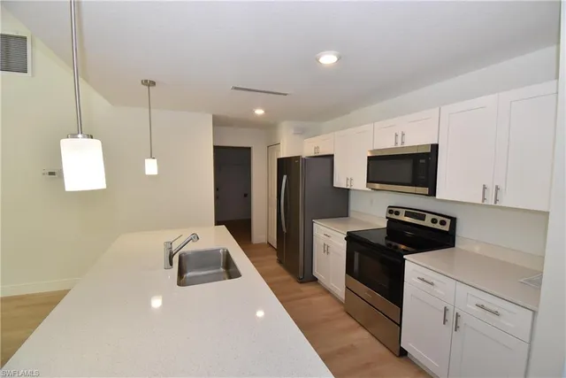 a kitchen with stainless steel appliances a stove a sink a microwave a refrigerator a stove and white cabinets