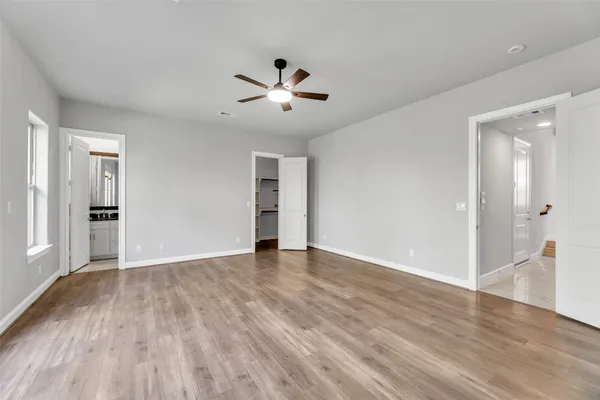 a view of an empty room with wooden floor and a ceiling fan