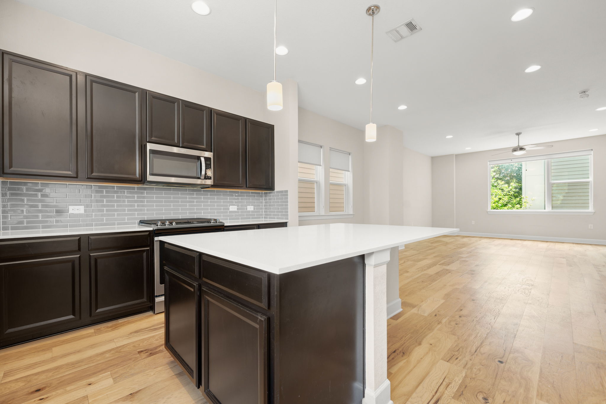 4403 Swift Path Austin, TX 78741 - Photo 6 of 32 Kitchen featuring dark wood cabinetry, a white countertop island, stainless steel microwave and range, and a light gray subway tile backsplash