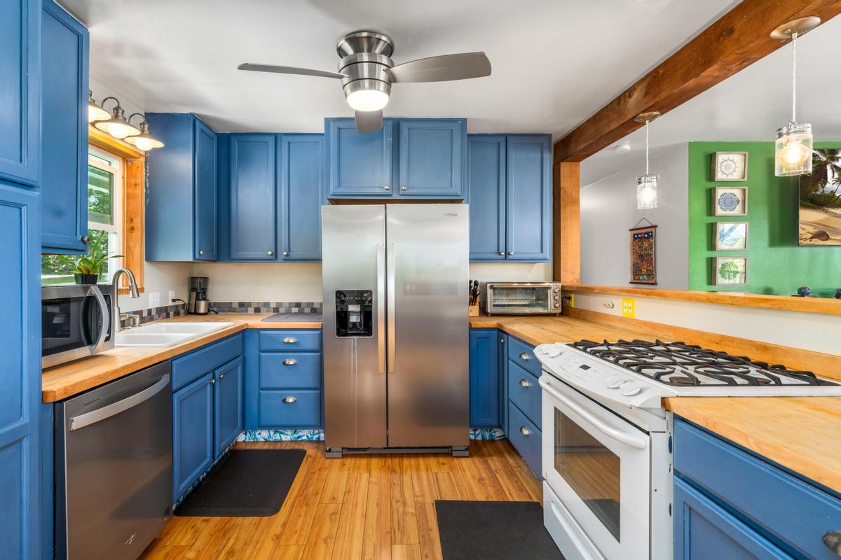 83-5434 Middle Keei Road Captain Cook, HI 96704 - Photo 10 of 30 a kitchen with stainless steel appliances granite countertop a refrigerator a sink dishwasher a stove and white countertops with wooden floor