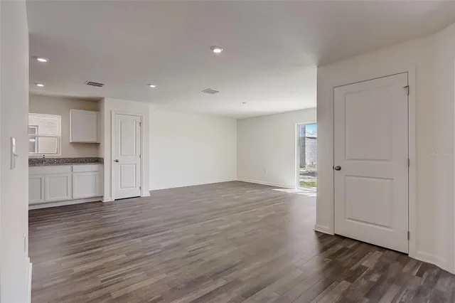 a view of empty room with wooden floor and kitchen