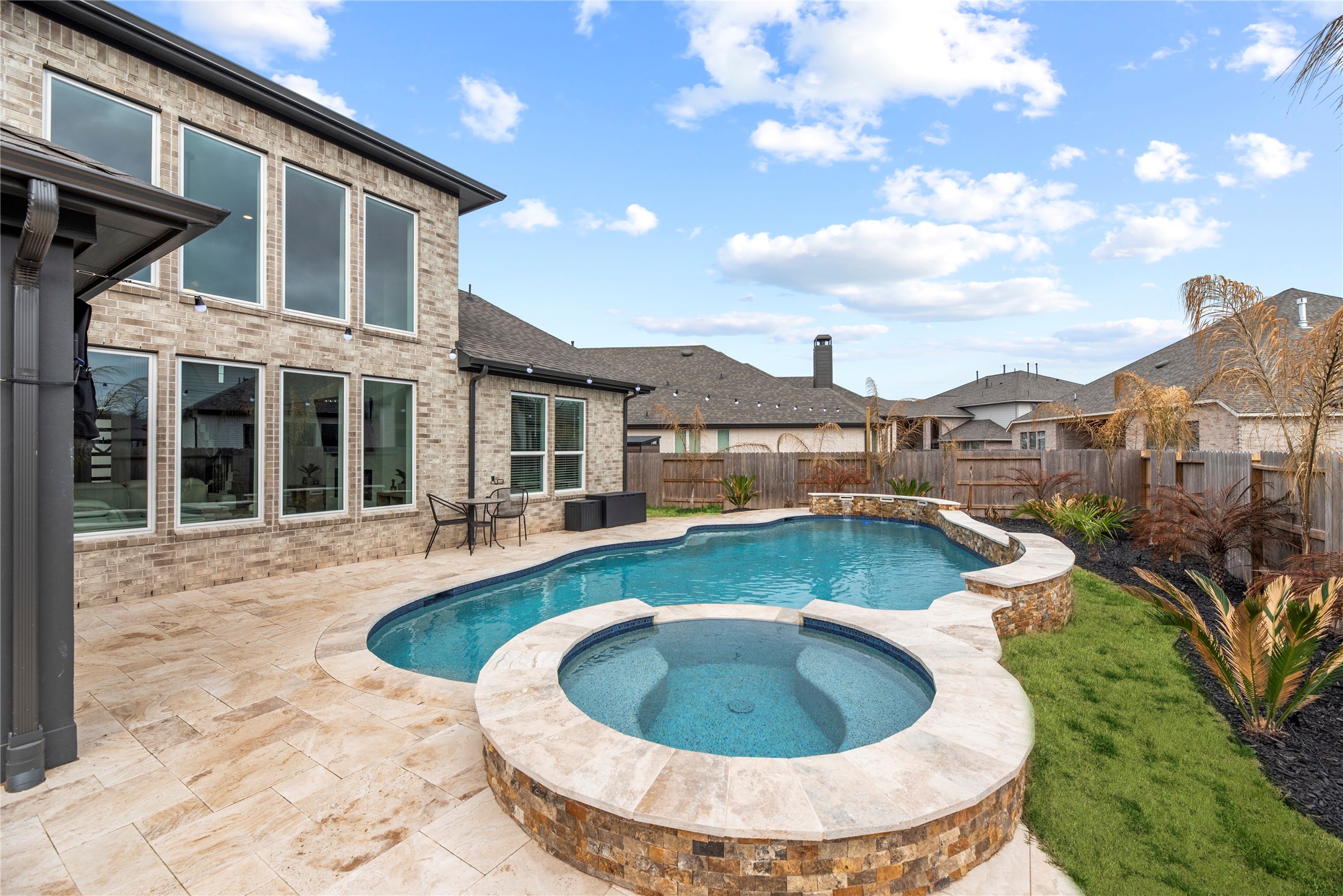 30155 GOLD FINCH Place Fulshear, TX 77441 - Photo 23 of 26 From this angle, the pool highlights the integrated raised spa, finished in stacked natural stone and complemented by travertine-style pavers that coordinate with the surrounding deck.