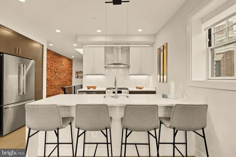 a kitchen with stainless steel appliances kitchen island granite countertop a dining table chairs and a refrigerator