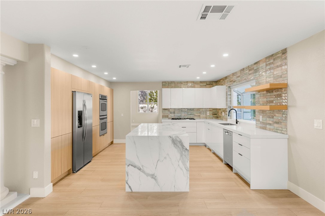 2104 Inverness Drive Henderson, NV 89074 - Photo 18 of 51 Kitchen featuring open shelves, light stone counters, appliances with stainless steel finishes, modern cabinets, and tasteful backsplash