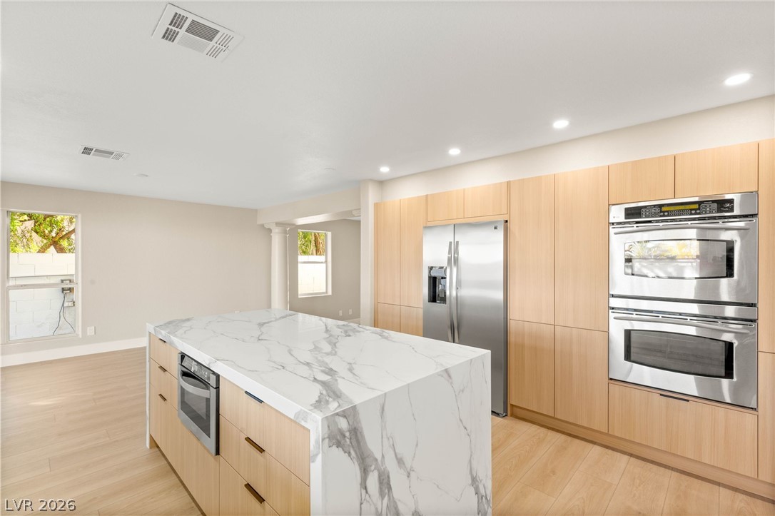 2104 Inverness Drive Henderson, NV 89074 - Photo 19 of 51 Kitchen featuring light brown cabinets, stainless steel appliances, modern cabinets, a center island, and light stone counters