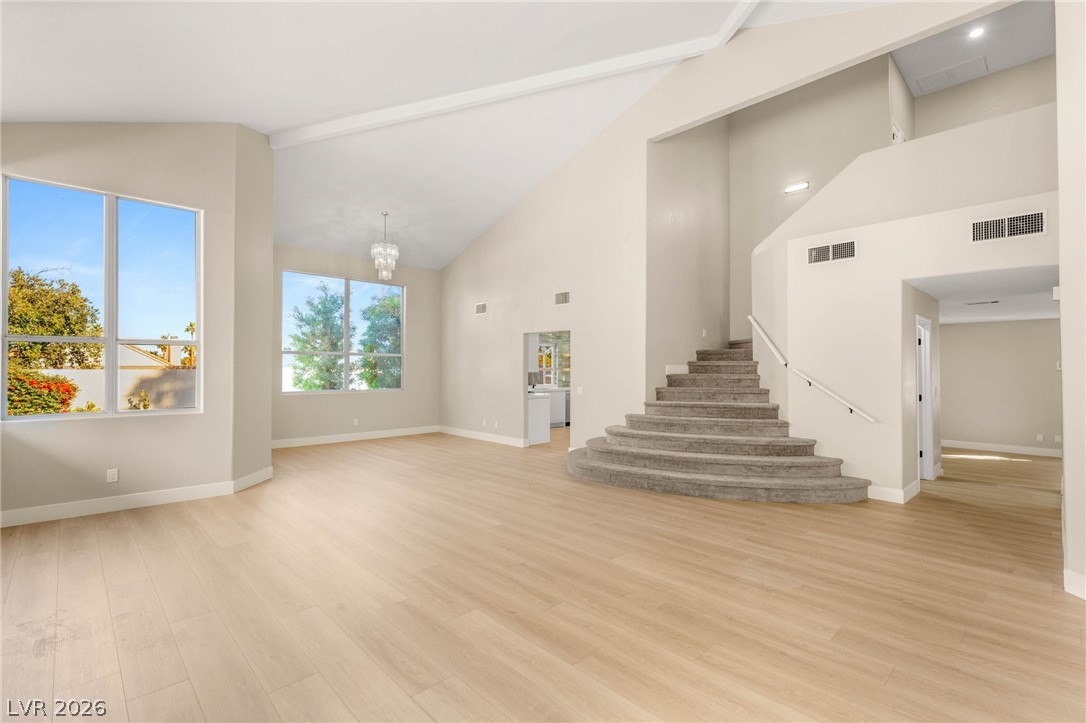 2104 Inverness Drive Henderson, NV 89074 - Photo 6 of 51 Unfurnished living room featuring a chandelier, light wood-type flooring, beamed ceiling, high vaulted ceiling, and stairs
