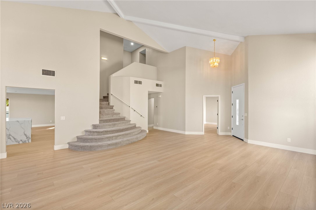 2104 Inverness Drive Henderson, NV 89074 - Photo 7 of 51 Unfurnished living room with light wood finished floors, beam ceiling, a chandelier, high vaulted ceiling, and stairs