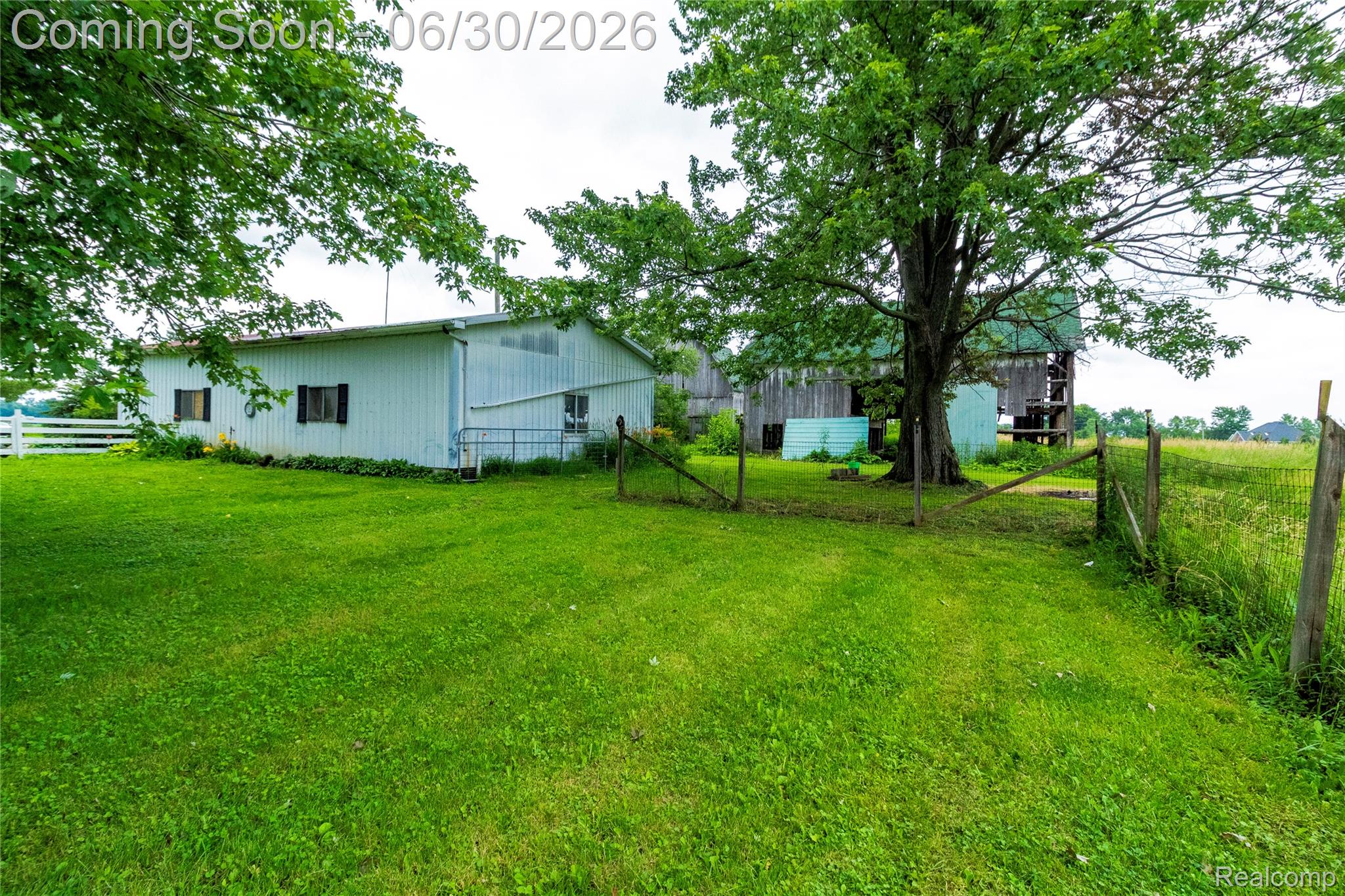 8150 Norman Road Imlay City, MI 48444 - Photo 43 of 58 Expansive green lawn with a white metal building featuring black-shuttered windows, complemented by mature trees and a rustic wire fence