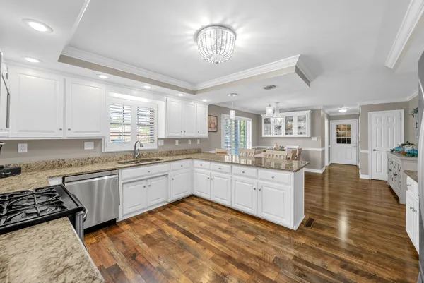 a large white kitchen with kitchen island granite countertop lots of white cabinets appliances and furniture