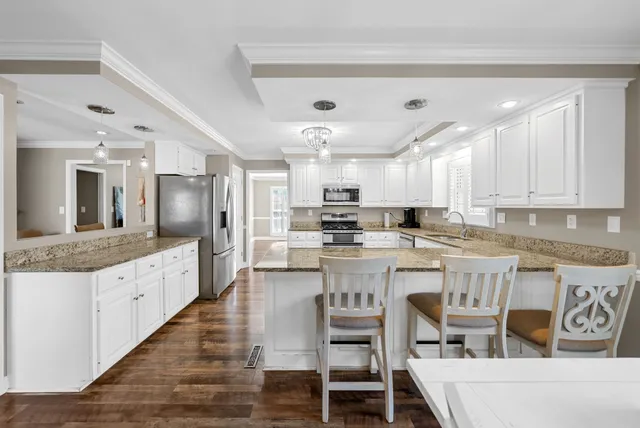a kitchen with granite countertop a refrigerator stove and white cabinets