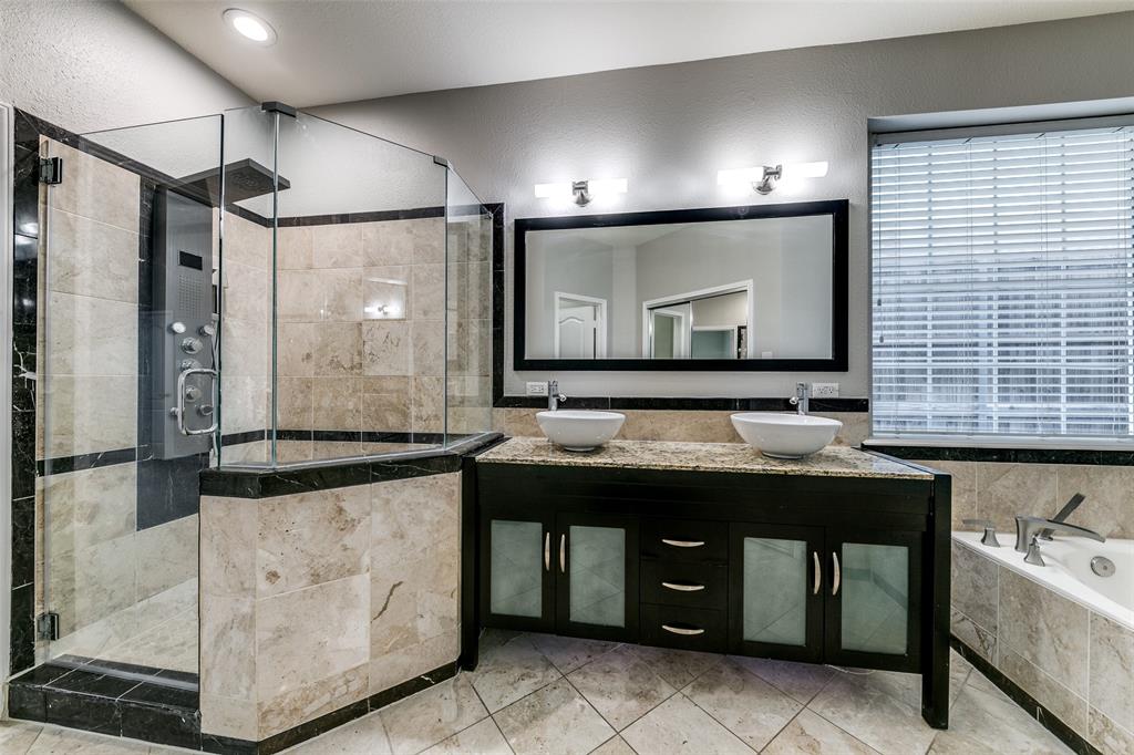 4532 Crown Ridge Drive Plano, TX 75024 - Photo 20 of 25 Spacious bathroom featuring a frameless glass shower enclosure with a multi-function shower panel, dual vessel sinks set on a granite-topped dark wood vanity, a deep soaking tub, and large format tiled flooring