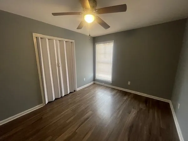 an empty room with wooden floor chandelier fan and windows