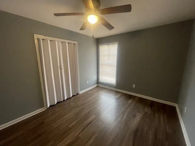 an empty room with wooden floor chandelier fan and windows