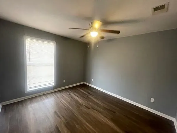 an empty room with wooden floor fan and windows