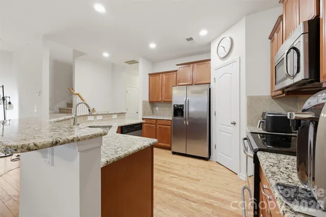 a kitchen with stainless steel appliances granite countertop a refrigerator a stove and a sink with wooden floor