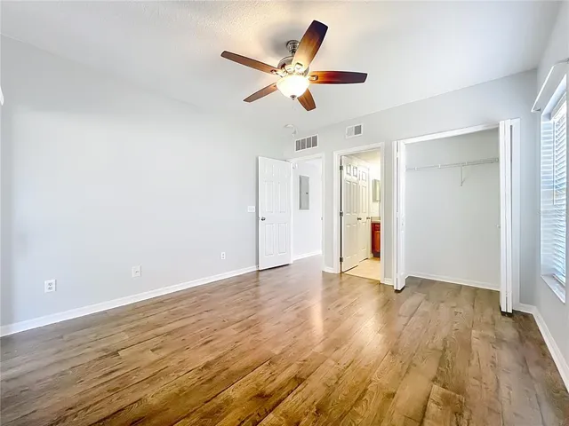 an empty room with wooden floor fan and windows