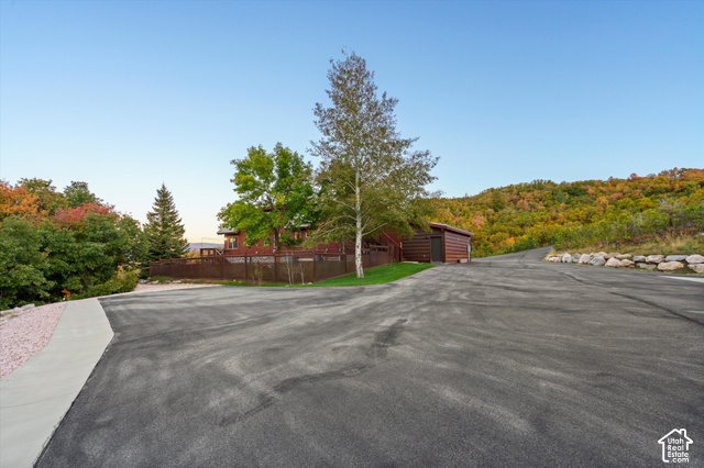 5878 Snowbasin Road Huntsville, UT 84317 - Photo 65 of 90 Asphalt driveway with an adjacent concrete walkway, leading to a log-style shed and a multi-level wood-sided residence, surrounded by mature trees and a natural rock retaining wall