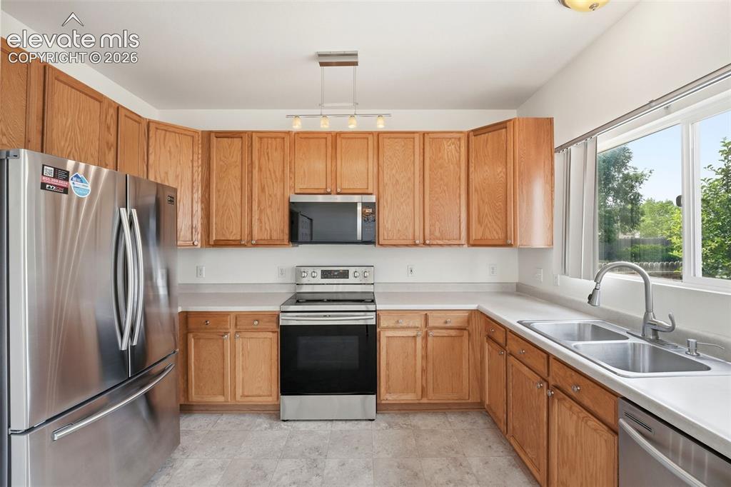 7904 Coffee Road Peyton, CO 80831 - Photo 11 of 48 Kitchen featuring wood cabinetry, stainless steel appliances, a double basin sink with a gooseneck faucet, light-toned countertops, and tile flooring