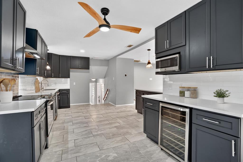 6609 Genoa Road Fort Worth, TX 76116 - Photo 15 of 40 Contemporary kitchen featuring dark cabinetry, stainless steel appliances, a built-in wine refrigerator, white countertops, and a subway tile backsplash
