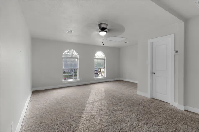 an empty room with chandelier fan and windows
