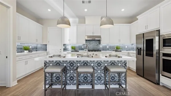 a large kitchen with kitchen island granite countertop a stove a sink a refrigerator and white cabinets with wooden floor