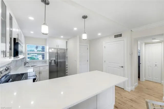 a large white kitchen with a refrigerator a sink dishwasher a oven and a dining table with wooden floor