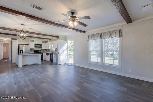 a view of an empty room with wooden floor and a kitchen