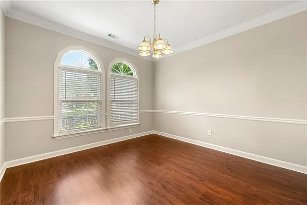 an empty room with wooden floor chandelier and windows